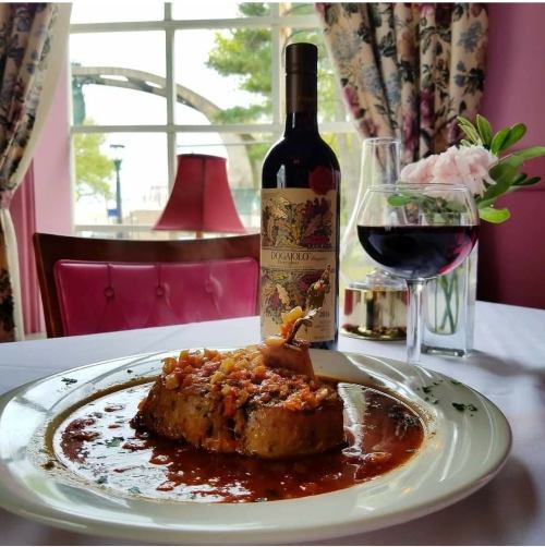 A plate of savory dish with sauce, accompanied by a glass of red wine and a bottle, set against a cozy dining backdrop.