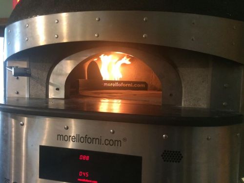 A wood-fired pizza oven with flames visible inside, featuring a digital display on the front.