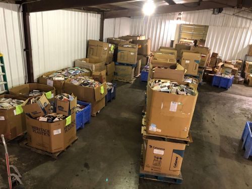 A warehouse filled with large boxes of books stacked on pallets, with some boxes open and books visible inside.
