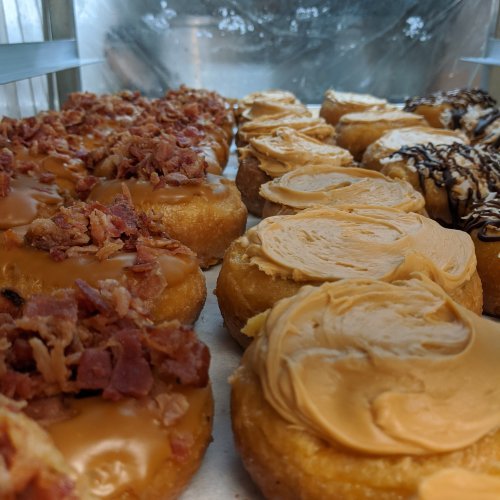 A display of donuts: some topped with bacon bits and caramel, others with creamy peanut butter and chocolate drizzle.
