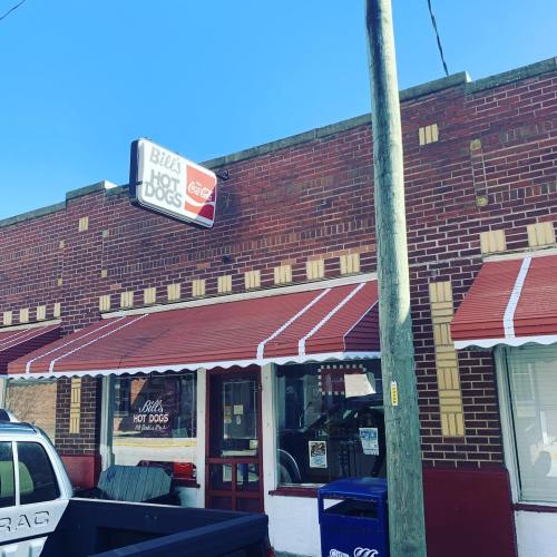Exterior of Bill's Hot Dogs restaurant with a red awning, sign, and a clear blue sky in the background.