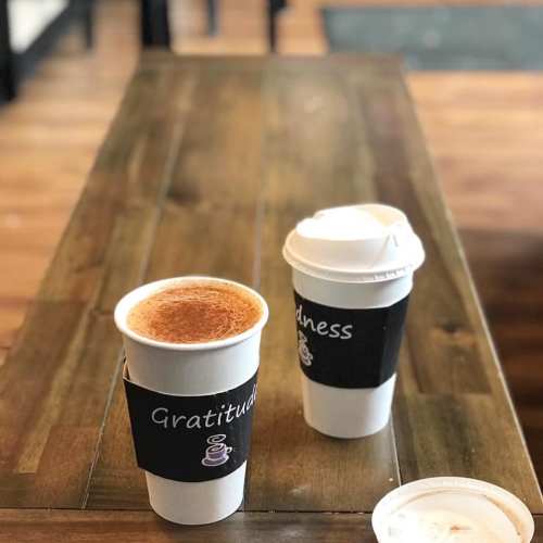 Two coffee cups on a wooden table, one labeled "Gratitude" and the other "Kindness."