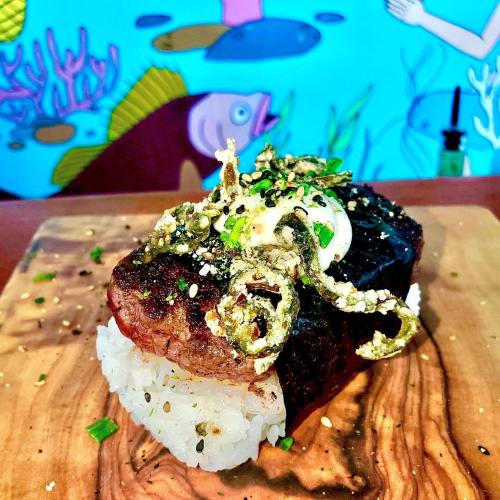A beautifully plated dish featuring a piece of steak on rice, topped with crispy onions and garnished with herbs.
