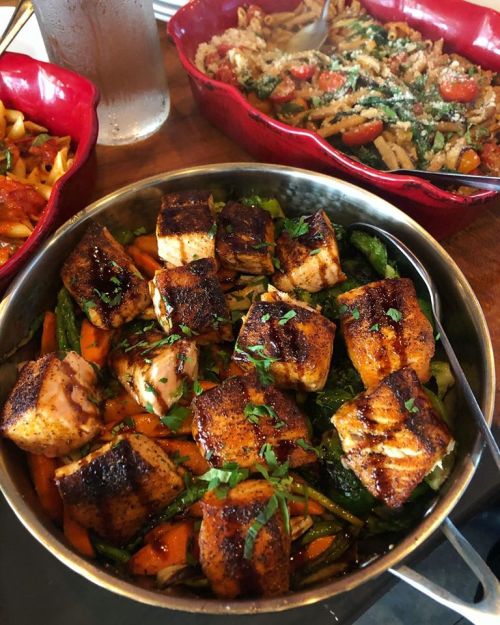 A dish of seasoned salmon fillets on a bed of sautéed vegetables, garnished with fresh herbs.