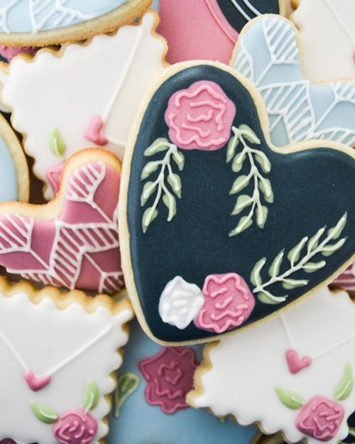 A variety of decorated cookies, including heart-shaped and envelope designs, featuring floral patterns and pastel colors.