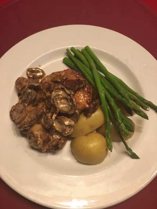 A plate featuring chicken with mushrooms, boiled potatoes, and steamed asparagus on a red tablecloth.