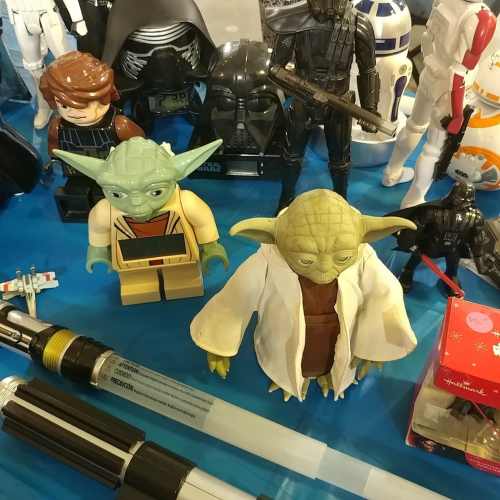 Two Yoda figurines in front of various Star Wars toys, including Darth Vader and R2-D2, on a blue table.