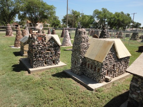 Miniature stone buildings with unique designs, set in a grassy area under a clear blue sky.