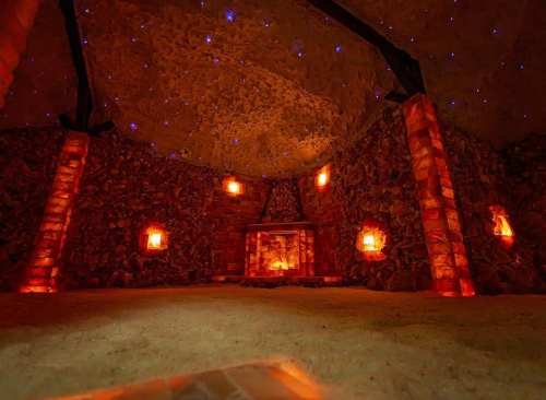 A serene salt cave with glowing orange lamps, a stone fireplace, and a starry ceiling, creating a calming atmosphere.