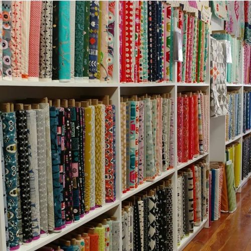 A colorful display of fabric rolls neatly arranged on shelves in a craft store.