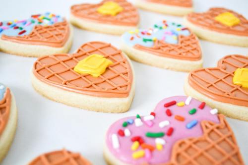 Decorated heart-shaped cookies with colorful icing and sprinkles, arranged on a white surface.
