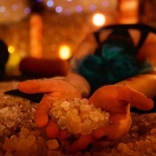 A person lies on the ground with hands open, holding small crystals in a serene, softly lit environment.