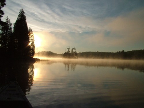 A serene lake at sunrise, with mist rising and trees silhouetted against a colorful sky.