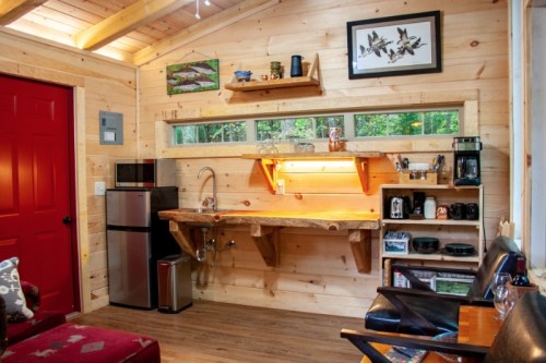 Cozy wooden interior featuring a kitchenette with a sink, coffee maker, and a red door. Natural light from windows.