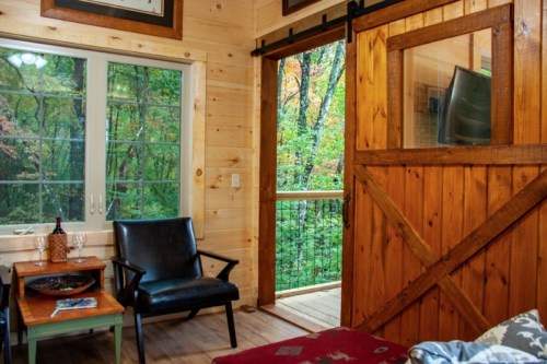 Cozy interior with wooden walls, a black chair, and a view of a forest through a sliding barn door.