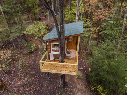 A cozy treehouse nestled in a forest, featuring a wooden exterior and a small balcony.