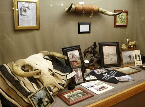 Display case featuring a cow skull, vintage photos, a saddle blanket, and decorative items related to Western culture.
