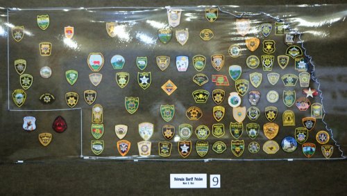 A display of various law enforcement patches from different counties in Nebraska, arranged on a map outline.
