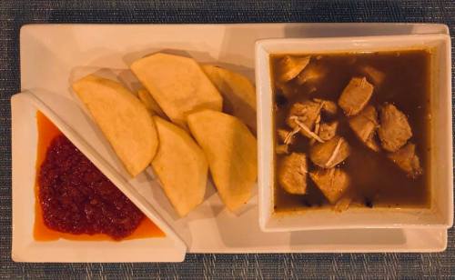 A plate with sliced potatoes, a bowl of chicken soup, and a side of red sauce.