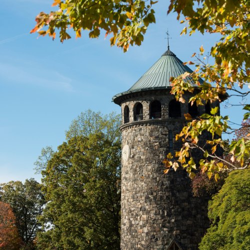 A stone tower with a green roof surrounded by trees under a clear blue sky.
