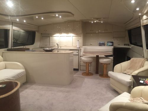 Interior of a luxurious yacht featuring a spacious lounge area, kitchen, and elegant seating. Soft lighting enhances the ambiance.
