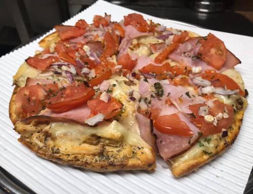 A freshly baked pizza topped with ham, tomatoes, onions, and herbs on a white paper plate.