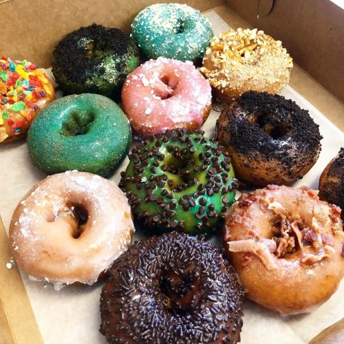 A variety of colorful donuts in a box, featuring sprinkles, frosting, and toppings like nuts and chocolate.
