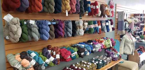 A colorful display of yarn skeins in various shades, neatly arranged on shelves and baskets in a craft store.