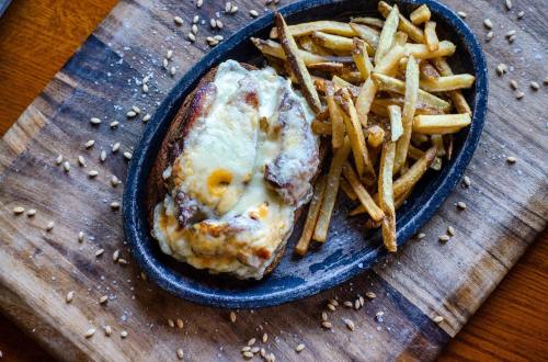 A sizzling plate with a cheesy sandwich and crispy fries, served on a wooden board with scattered sesame seeds.