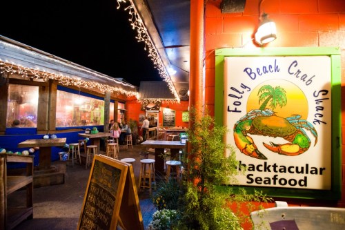 A vibrant seafood restaurant exterior at night, featuring a colorful sign and string lights, with patrons enjoying the atmosphere.