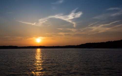 A serene sunset over a calm lake, with golden reflections on the water and wispy clouds in the sky.