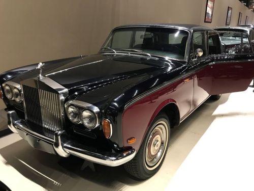 A classic black and burgundy Rolls-Royce with a shiny chrome grille, parked indoors with an open door.