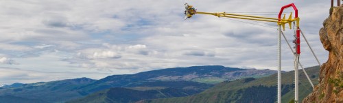 A thrill ride extends over a mountainous landscape, with riders suspended in the air against a cloudy sky.