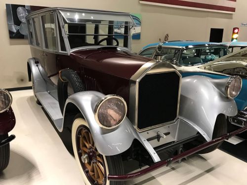 A vintage car with a maroon and silver exterior, featuring a classic design and large headlights, displayed in a museum.