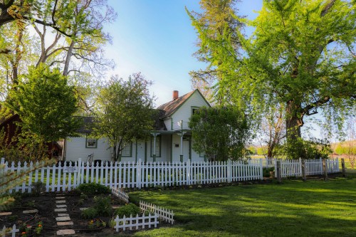 A charming white house surrounded by a white picket fence, lush greenery, and a well-maintained garden.