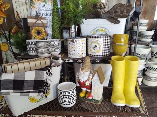 A display of decorative garden items, including pots, a gnome, and yellow rain boots, arranged on a rustic shelf.