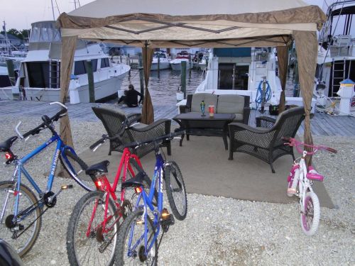 A cozy outdoor seating area under a canopy, with bicycles parked nearby and boats in the marina in the background.