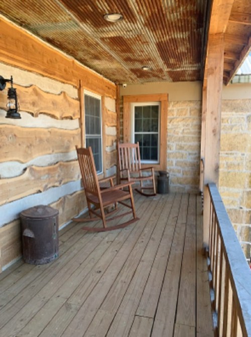 A rustic porch with two rocking chairs, wooden walls, and a lantern, creating a cozy outdoor space.