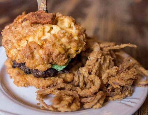 A decadent burger topped with macaroni and cheese, served with crispy fried onions on the side.