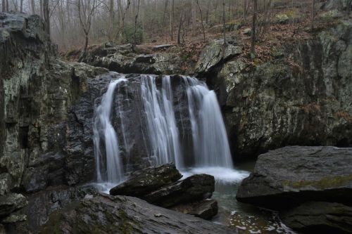 A serene waterfall cascading over rocky terrain, surrounded by trees and a misty atmosphere.