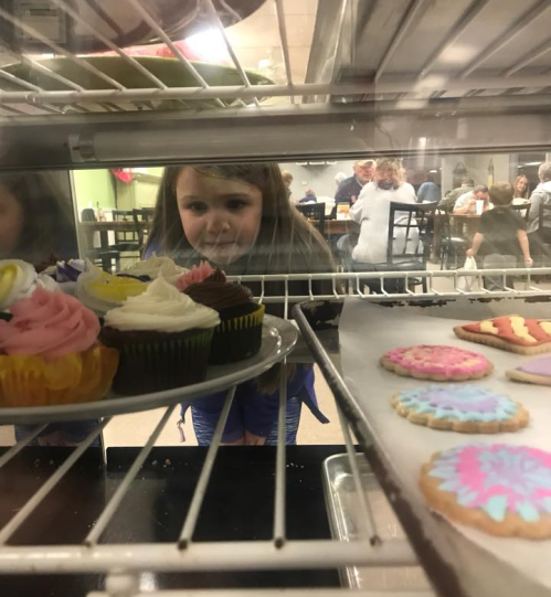 A child gazes longingly at colorful cupcakes and cookies displayed in a bakery case.