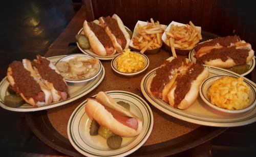A tray with multiple hot dogs topped with chili, sides of fries, macaroni and cheese, and pickles.