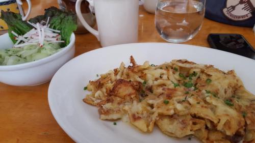 A plate of cheesy baked pasta with chives, accompanied by a side salad of lettuce, radishes, and cucumber.