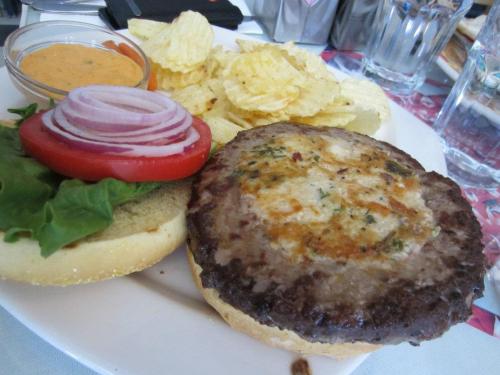 A plate with a burger patty, lettuce, tomato, red onion, and a side of potato chips with dipping sauce.
