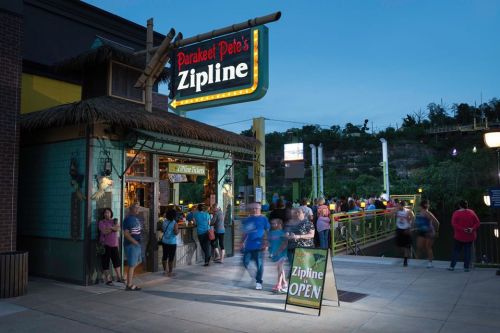 A lively entrance to Parakeet Pete's Zipline at dusk, with people gathered and a sign indicating it's open.