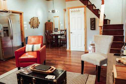 Cozy living space featuring red and gray chairs, a wooden dining table, and a staircase in a warm, inviting atmosphere.