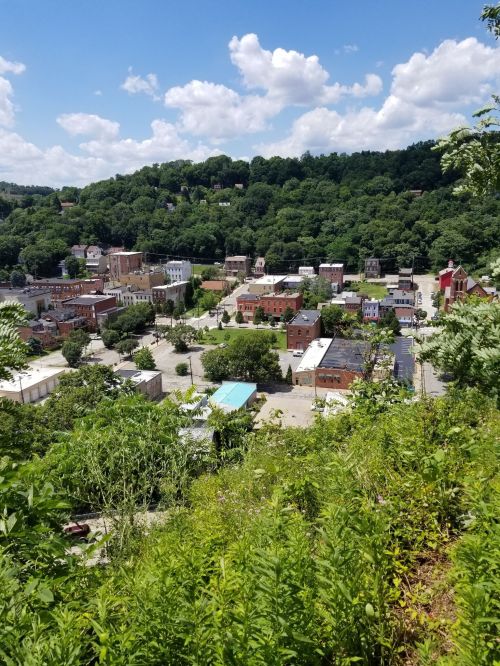 Aerial view of a small town surrounded by lush green hills under a bright blue sky with scattered clouds.
