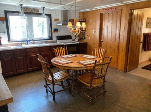 Cozy kitchen with wooden cabinets, a round table with chairs, and a pantry door in a rustic setting.