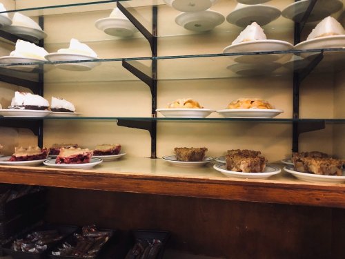 A display case filled with various slices of pie and dessert on white plates, arranged on glass shelves.