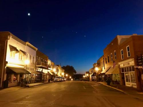Quiet street scene at dusk, with charming shops and warm lights under a deep blue sky.